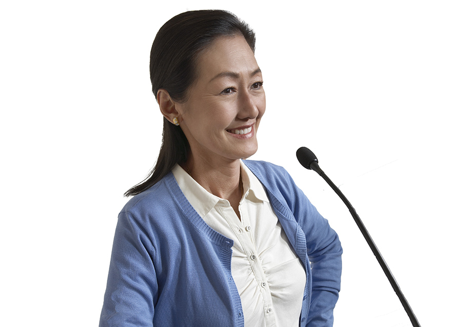 Chinese conference interpreter speaking on the microphone smiling wearing a blue cardigan